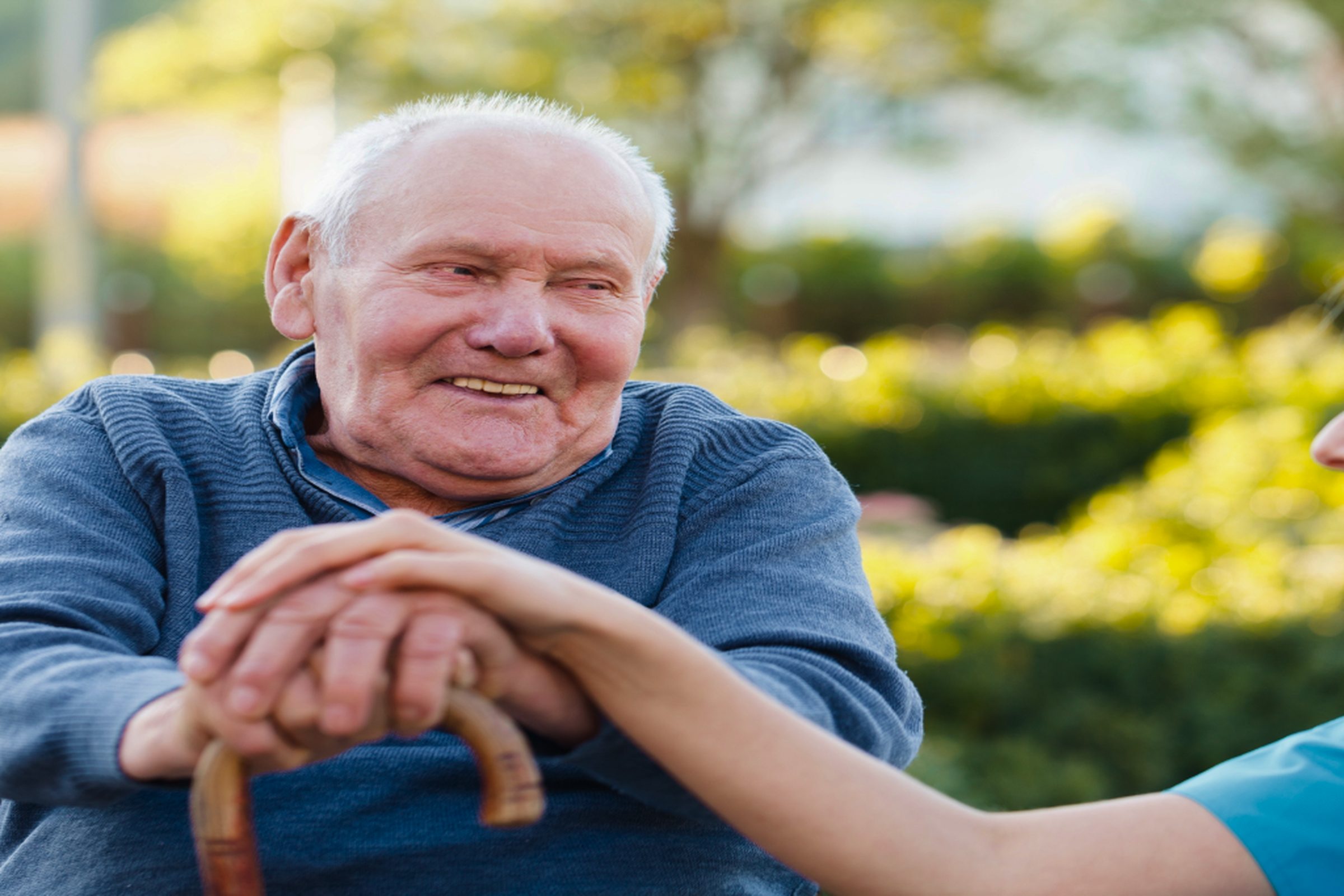 A resident smiling outdoors with a carer’s hand on his