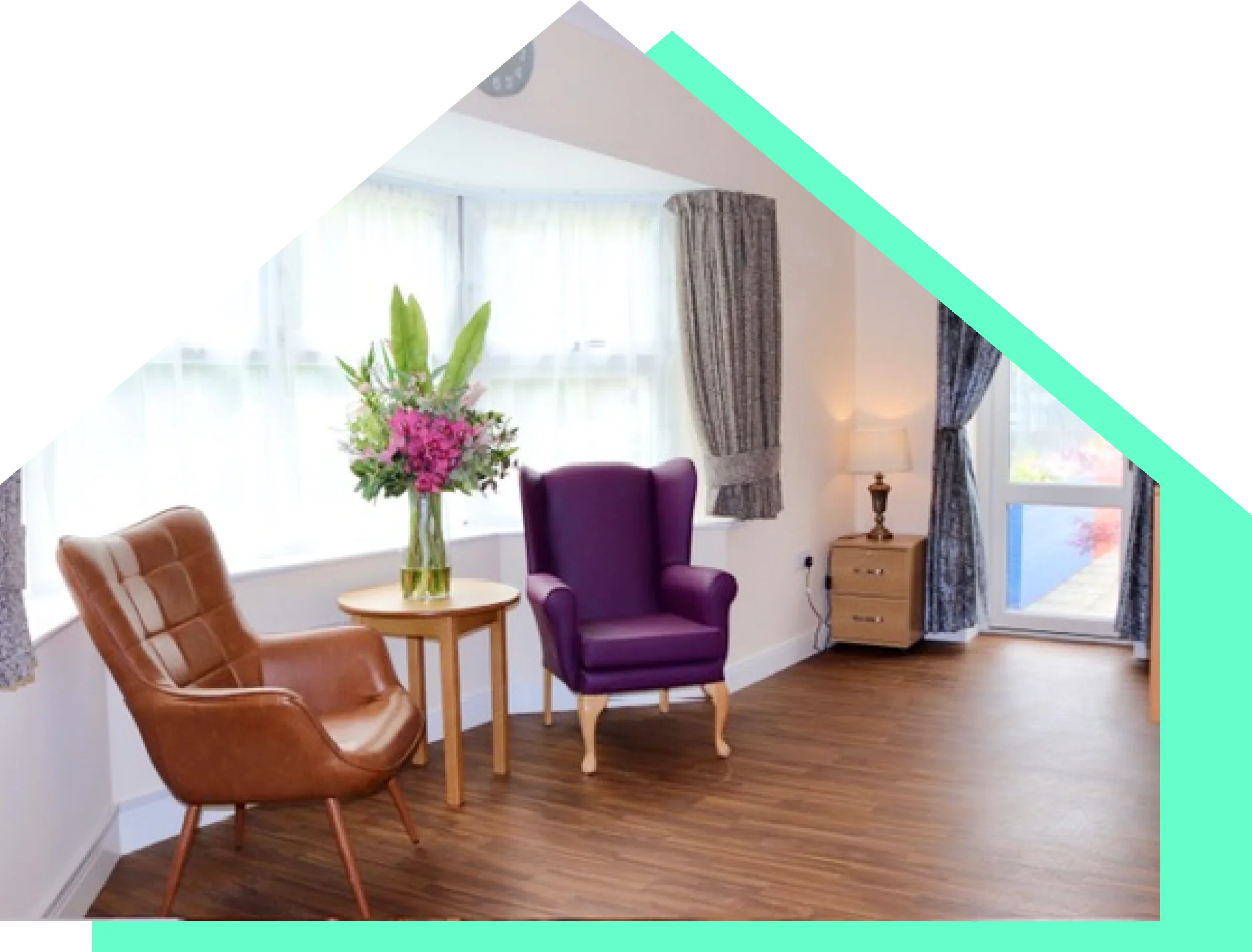 A resident lounge at Lola’s House with a bay window, armchairs and fresh flowers